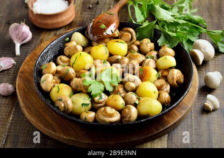 Delicious fried mushrooms with potatoes in cast iron pan on wooden background Stock Photo
