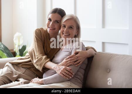 Portrait happy adult daughter and older mother sitting on couch Stock Photo
