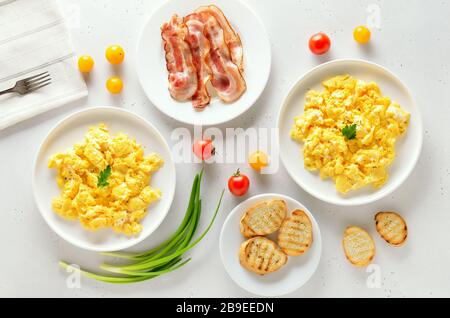 Healthy diet breakfast concept. Scrambled eggs, bacon and tomatoes over white stone background. Top view, flat lay Stock Photo