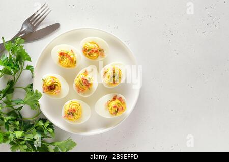 Stuffed eggs with egg yolk, bacon, mustard on plate over light stone background with free text space. Healthy diet food for breakfast. Top view, flat Stock Photo