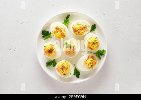 Deviled stuffed eggs with egg yolk, bacon, mustard and parsley. Healthy diet food for breakfast. Top view, flat lay. Stock Photo