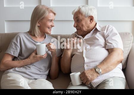 Happy older wife and husband talking, drinking hot drinks Stock Photo