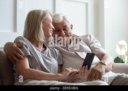 Happy older woman and man hugging, using phone together Stock Photo