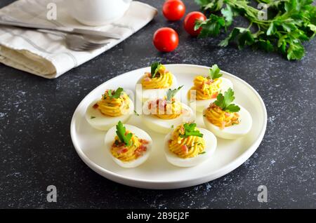 Deviled stuffed eggs with egg yolk, bacon, mustard and parsley on dark stone background Stock Photo
