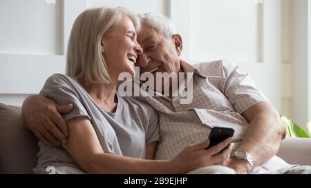 Happy older wife and husband cuddling, using phone together Stock Photo