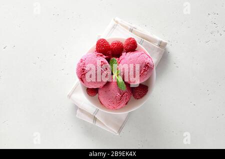 Raspberry ice cream scoop with fresh raspberries in bowl over white stone background with free text space. Top view, flat lay Stock Photo