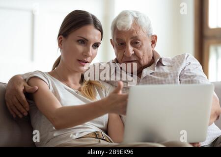 Serious adult daughter helping older father with laptop close up Stock Photo