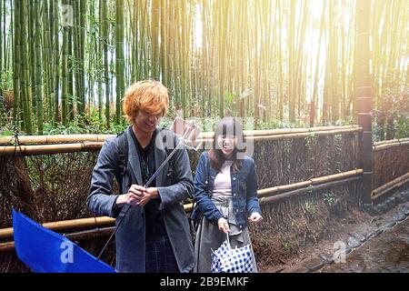 Kyoto, Japan - 03.17.20 Happy young beautiful Japanese couple take a selfie in bamboo forest. The bamboo groves of Arashiyama, Kyoto, Japan. Arashiyama is a district on the western outskirts of Kyoto. Stock Photo