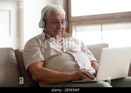 Smiling older man wearing headphones using laptop at home Stock Photo