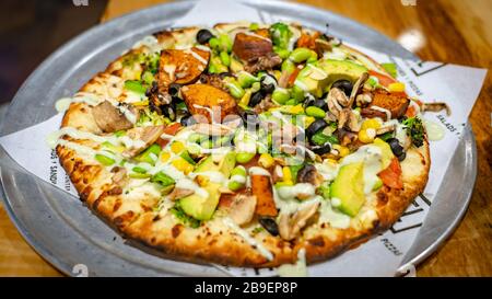 Pizza topped with black olives, mushrooms, golden corn, broccoli, avocado, edamame, and sweet potatoes Stock Photo