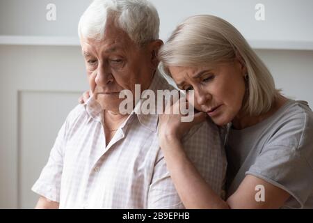 Unhappy middle-aged wife supporting and comforting older husband Stock Photo