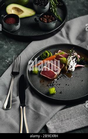Tuna tagliata in vegetables stewed carrots and peppers, Beautiful serving, traditional Italian cuisine, gray background, copy space. food concept. Stock Photo