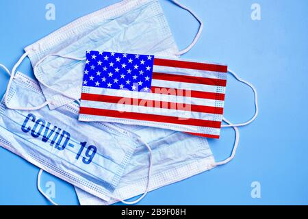 Medical masks on a blue background with the image of the American flag and the inscription covid-19. Concept of a virus epidemic in a country. Close u Stock Photo