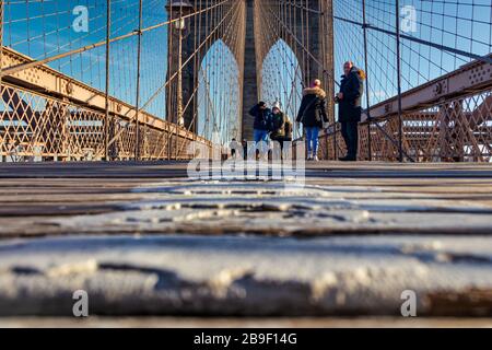 Brooklyn Bridge in NYC daylight view low angle shot with people walking on the bridge and clouds in sky in background