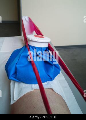 Rehabilitation with Elastic Red Band and Ice on the Knee on the Physiotherapy Bed within a Medical Centre. Stock Photo