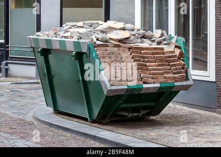 Neat industrial skip parked on the clean sidewalk full loaded with bricks and rubble in Dordrecht in the Netherlands Stock Photo