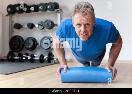 Mature man doing press-ups in a gym with barbells in the background Stock Photo