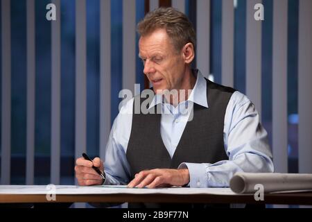 Mature businessman, architect or engineer  working at home at a desk late at night - focus on the face Stock Photo
