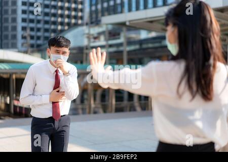 Asian ill businessman cough with mask and businesswoman stop sign hand him to keep distance protect from COVID-19 viruses and people social distancing