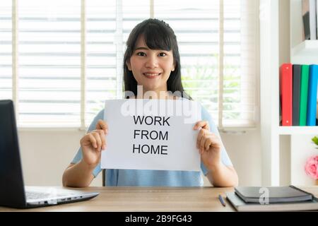 Asian Business woman holding sheet of paper with text work from home for protect virus and take care of their health from COVID-19. Working at home co Stock Photo