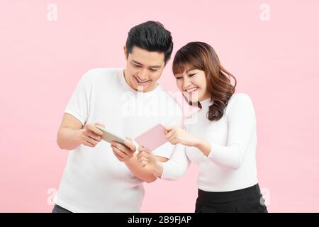 Image of funny young couple man and woman peeking at each others cell phones holding in hands isolated over pink background Stock Photo