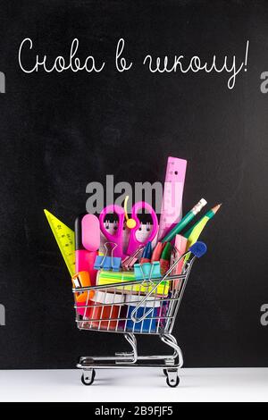 Shopping cart with school supplies over chalkboard background. School supplies in a shopping trolley. Back to school Education concept Stock Photo