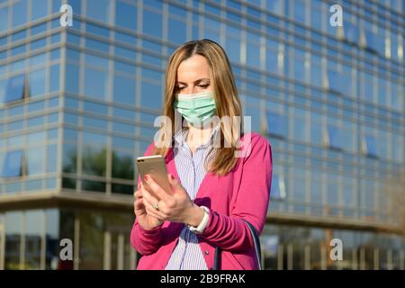 Coronavirus epidemic, woman wearing a protective face mask and using a smartphone in a city street as the number of Covid 19 virus cases across Europe Stock Photo