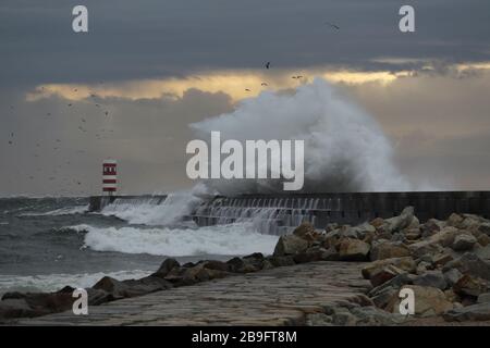 Dramatic stormy winter sunset at the Douro river mouth with big wave splash against north pier and beacon. Stock Photo