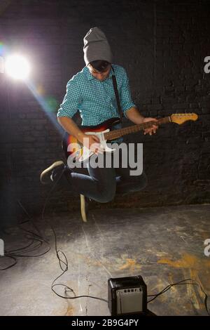 Teenage boy playing electric guitar, jumping above amplifier Stock Photo