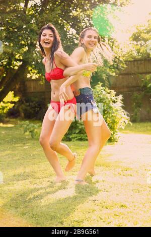 Portrait playful teenage girls in bikinis arm in arm in sunny summer backyard Stock Photo