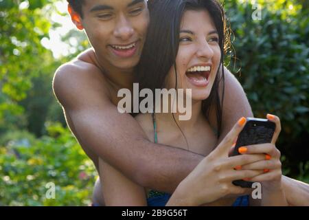 Happy, affectionate young couple using smart phone on summer patio Stock Photo