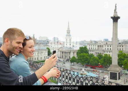 Happy couple using camera phone above Trafalgar Square, London, UK Stock Photo