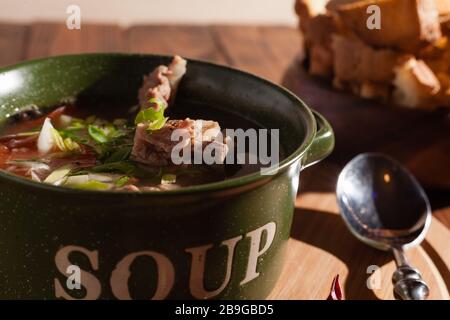 Rustic meat bone soup / broth sprinkled with green onions on a wooden table with crackers. Stock Photo