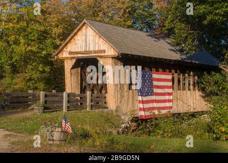 The Cilleyville Bog covered bridge, built in 1887 in the town lattice truss style spans Pleasant Brook in Andover, NH. It is draped with a large Ameri Stock Photo