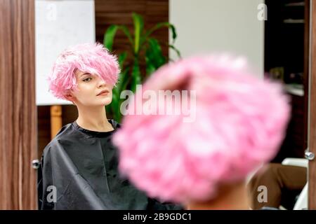 Woman with pink hair looking in the mirror at hair salon. Stock Photo