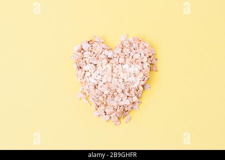 Oat flakes on a yellow background. Heart shaped symbol. Healthy eating concept. Stock Photo