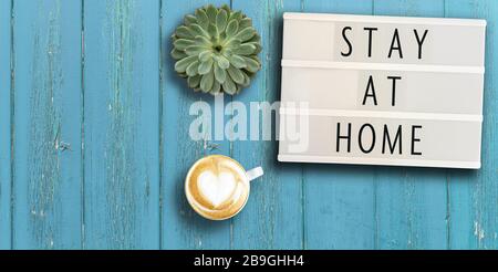 lightbox with appeal text STAY AT HOME on rustic wooden table with potted plant and coffee, social distancing concept during coronavirus pandemic Stock Photo