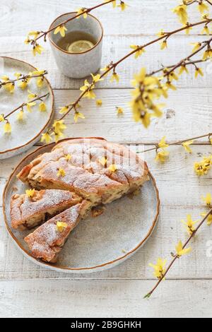 Home baked apple pie with yellow forsythia blooms on a white wooden table. Spring table setting Stock Photo