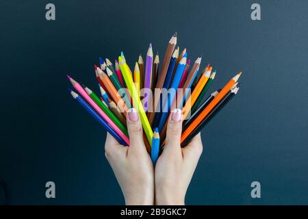 bunch of colored pencils in hand. A woman's hand holds a set of colored pencils on a black background Stock Photo