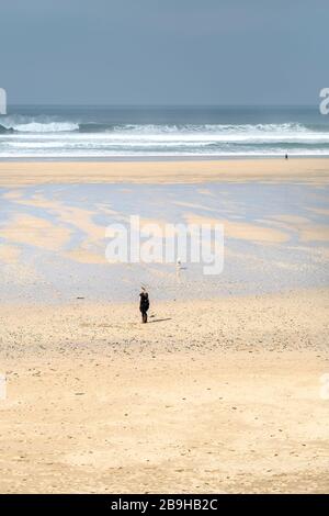 Newquay, Cornwall, UK. 24th March, 2020.  Local residents taking the Government advice and ensuring there is a 2 metre distance between them as they enjoy a deserted Fistral Beach in Newquay in Cornwall.   Gordon Scammell/Alamy Live News. Stock Photo