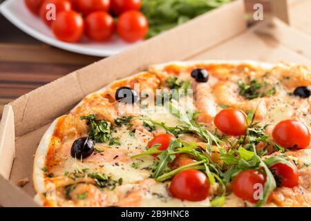 Tasty italian pizza with salmon in cardboard box on a table close up Stock Photo