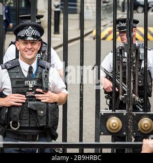 Armed Guards. A friendly London policeman standing guard outside the gates of Downing Street with armed colleagues in the background. Stock Photo