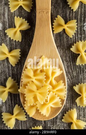 Farfalle pasta on wooden spoon. Uncooked pasta on rustic background. Top view Stock Photo