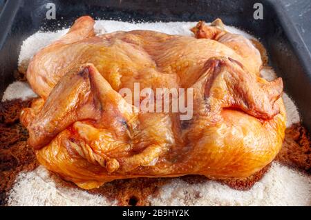 Chicken baked in the oven on a thick layer of salt on a metal tray Stock Photo
