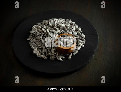 Unpeeled sunflowers seeds salted sunflower seeds on black wood Stock Photo
