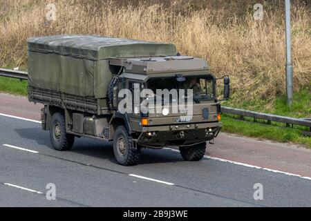 British Army green dropside General Service truck, canvas-covered MAN HX60 18.330 4x4 Military vehicle towing a trailer; travelling on the M6 Motorway UK Stock Photo