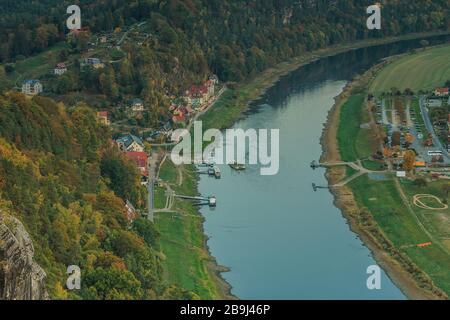 Viewpoint from the Bastei bridge in the evening. River Elbe with a view of the spa town of Rathen. Rocks and trees in autumn. Buildings, ship, ferry Stock Photo