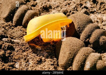 Used yellow toy boat lying upside down between sand shells on the sandy ground in the sun. Seen in Germany in March. Stock Photo
