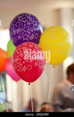 Three colourful 18th birthday party balloons, red, purple and yellow, at a party Stock Photo