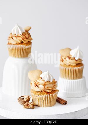 Carrot cupcakes with caramel, walnuts and spices decorated with heart shaped biscuit, meringue and salty caramel on white background. Free space for y Stock Photo